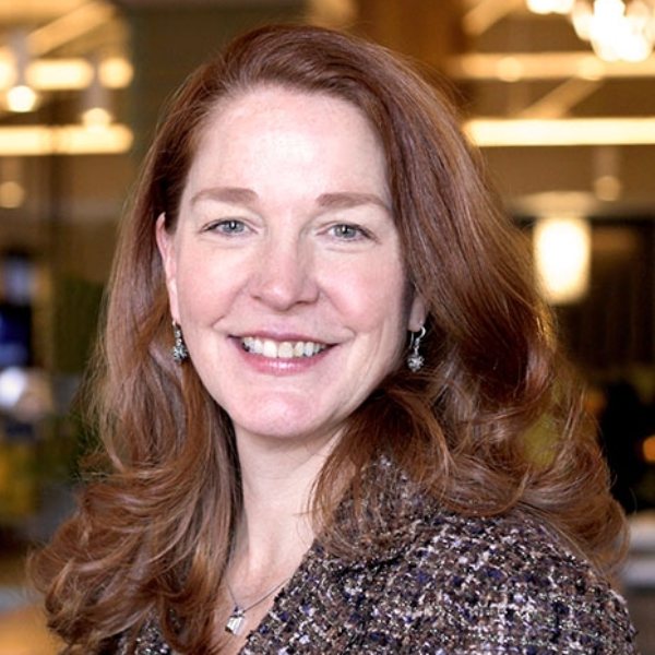 Headshot for Erin Hyer - a white woman with long red hair, smiling with a patterned suit jacket and drop earrings