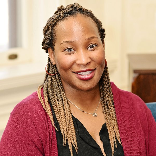 Headshot for Iheoma Iruka - a Black woman with tan and brown braids, smiling with red lipstick and a red sweater