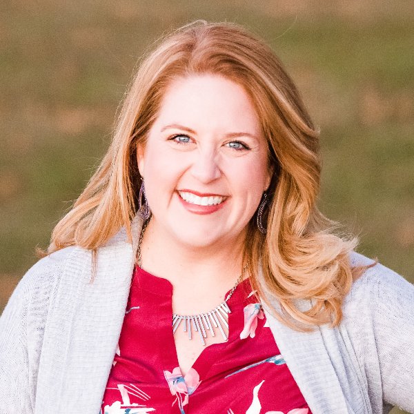 Headshot for Jamie White - white woman with strawberry blond long hair, smiling in a red top with tan sweater