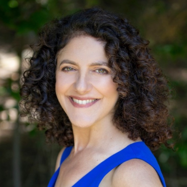 Headshot for Julie Kurtz - white woman with curly brown hair looking over her shoulder, smiling big, in a bright blue top