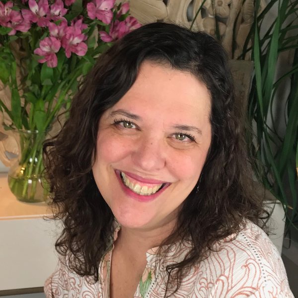 Headshot for Sally Haughey - white woman with medium brown hair, smiling over shoulder at camera, white floral top