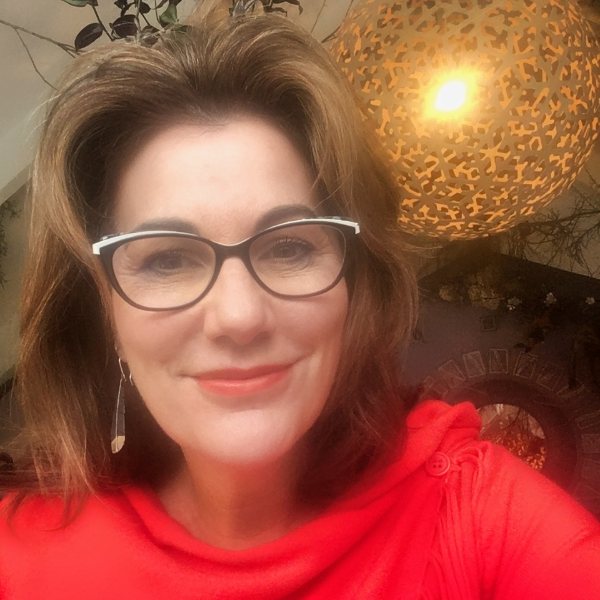 Headshot for Toni Christie - white woman with brown hair, glasses, soft smile, red lips and bright red sweater