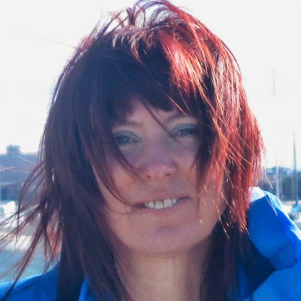 Headshot for Trisha Lee - white woman, bright red short hair, smiling, in a blue jacket standing outside