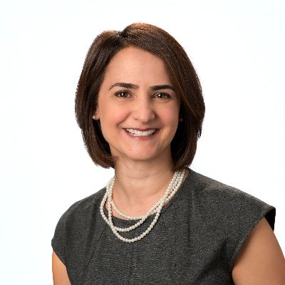 Headshot for Elizabeth - a light-skinned woman with brown hair, brown eyes, smiling, wearing pearls & a grey top