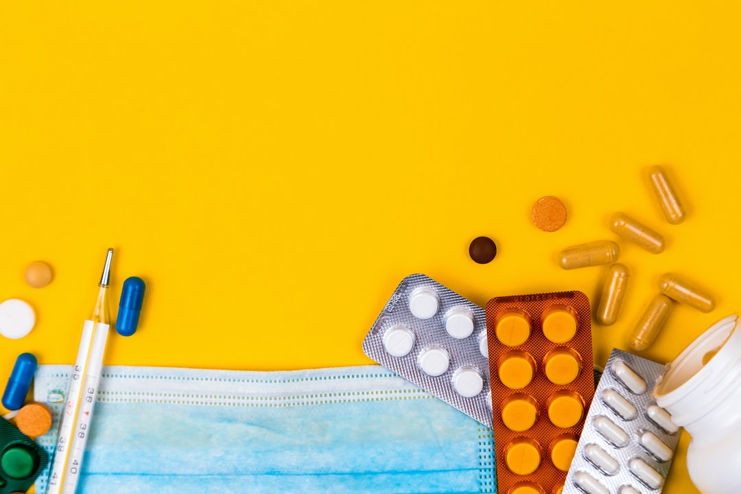 Multiple tablets, some packets and some loose, with a blue face mask, across the lower half of image. Yellow background