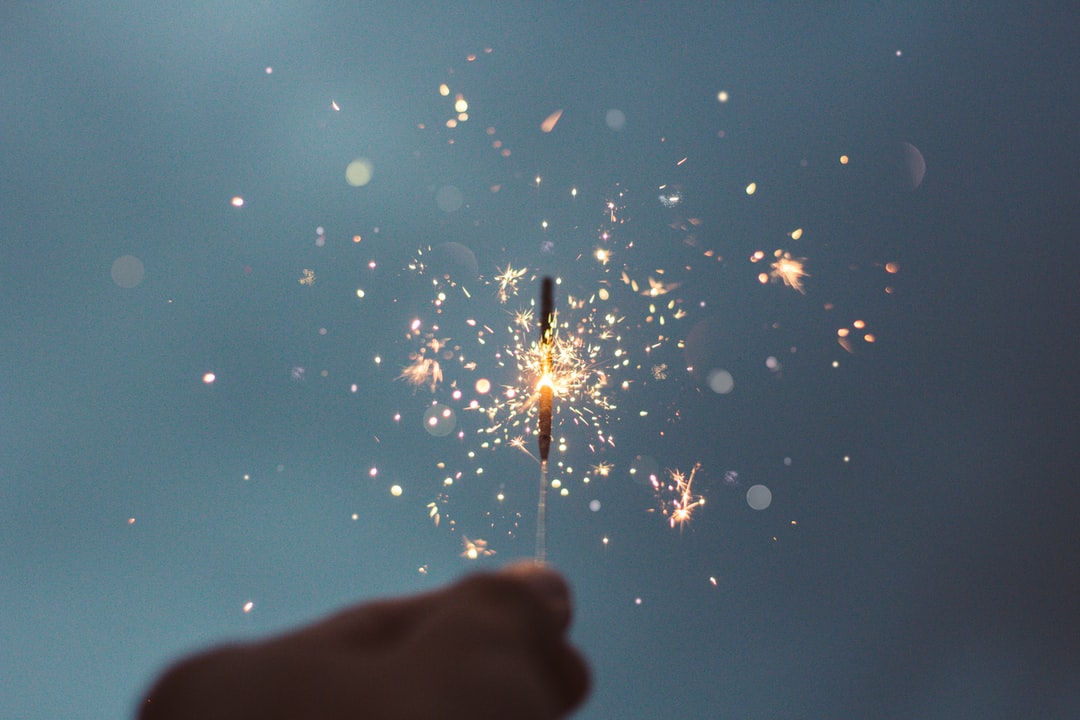 Photo of a sparkler. Dark blue / grey background, with the sparkler centrally & sparks in all directions