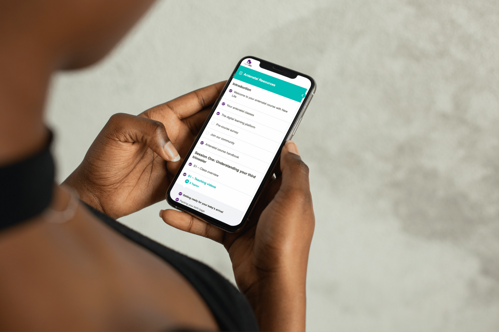 photo of person of colours hands holding mobile phone with screen showing the preparing for your baby's arrival course