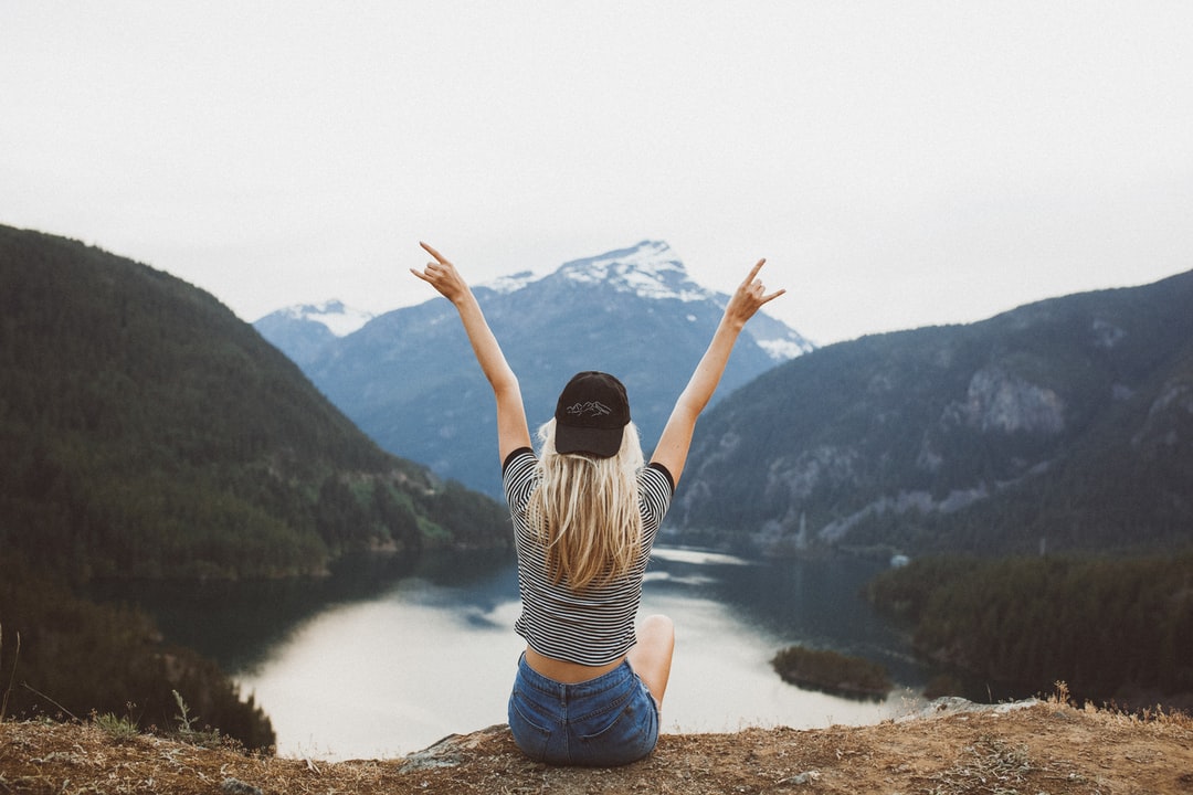 Woman sitting above a lake enclosed by low hills with her arms up in the air