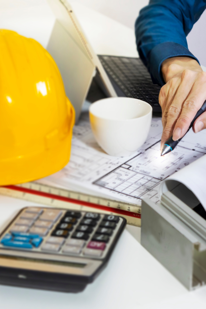 Construction business owner calculating budget with a calculator, blueprint and hard hat on the side