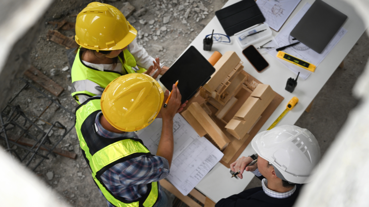 Top view of construction owner and contractors reviewing construction plans and a building model at a construction site table