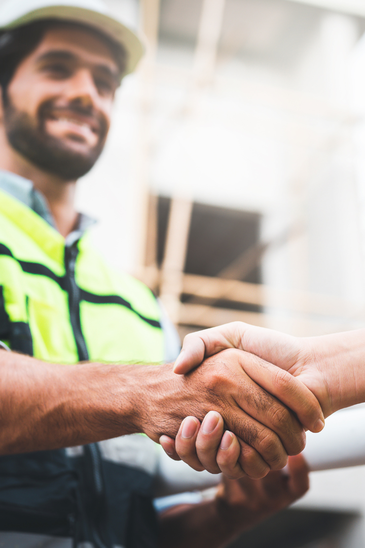 Male construction worker smiling and shaking hands with partner
