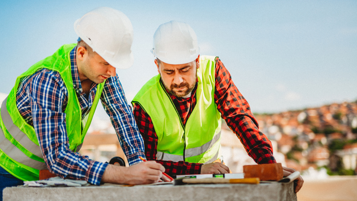 Two construction workers at a construction site looking at plans