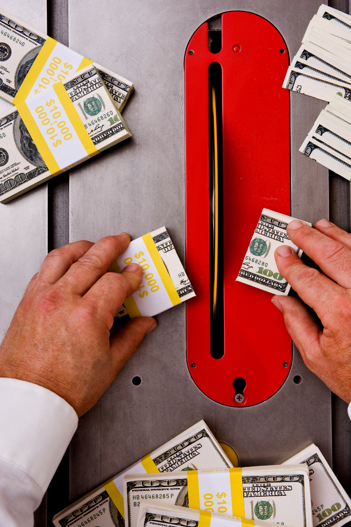 Construction owner cutting stacks of $100 bills on a table saw