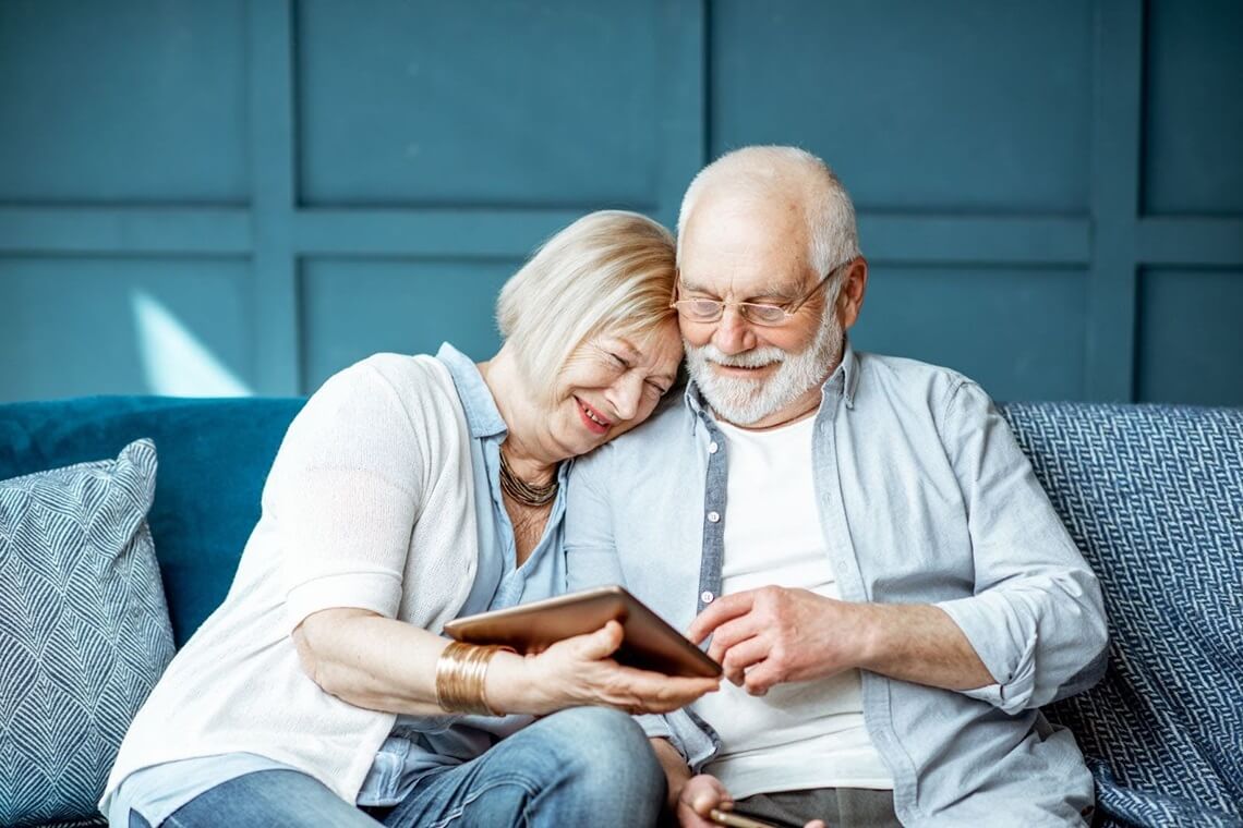 a senior couple sitting on the couch and looking at the tablet