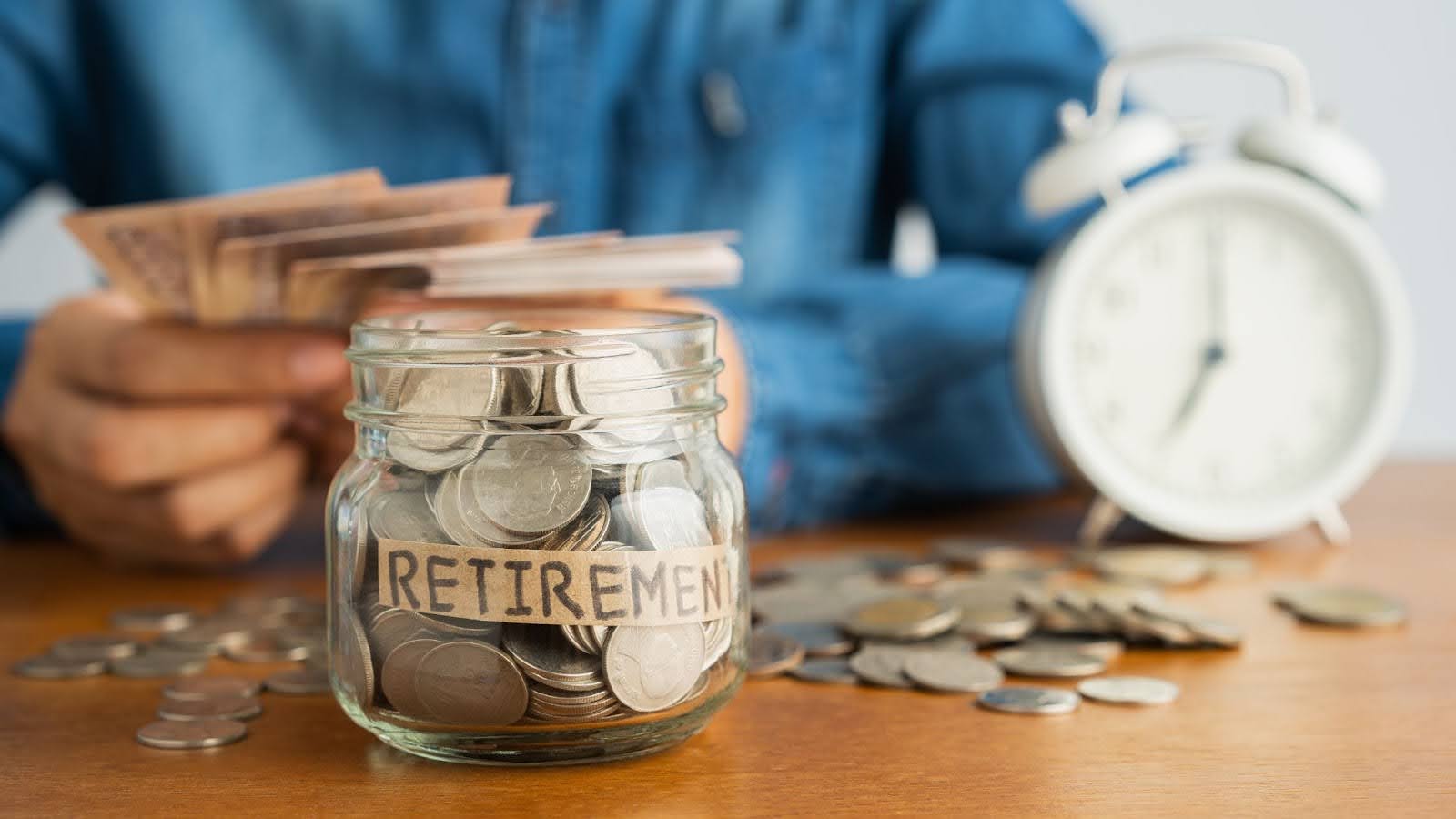 a glass jar with “retirement” written on it next to a man, an alarm clock, and a pile of coins