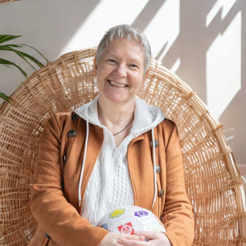 Karen Peters smiling, sat in a wicker chair holding the Cognomovement ball in her lap.