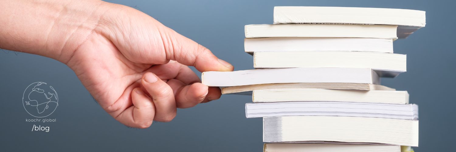 Hand pulling out a single book from the middle of a pile of unidentifiable books