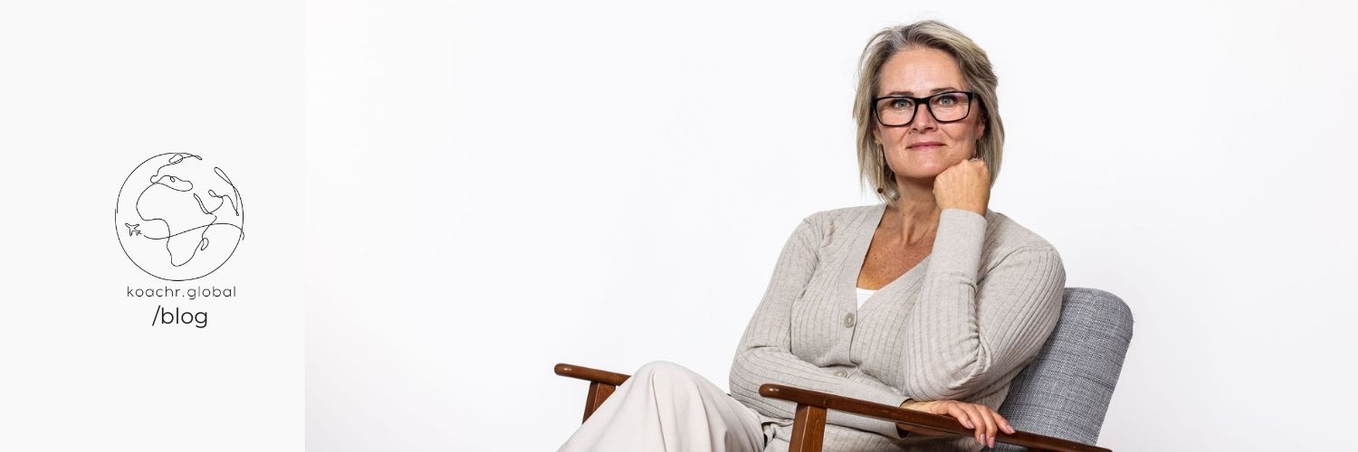 Portrait of Impact Career Coach Veronika Ambertson, sitting in armchair, legs crossed, and resting her chin on her hand.