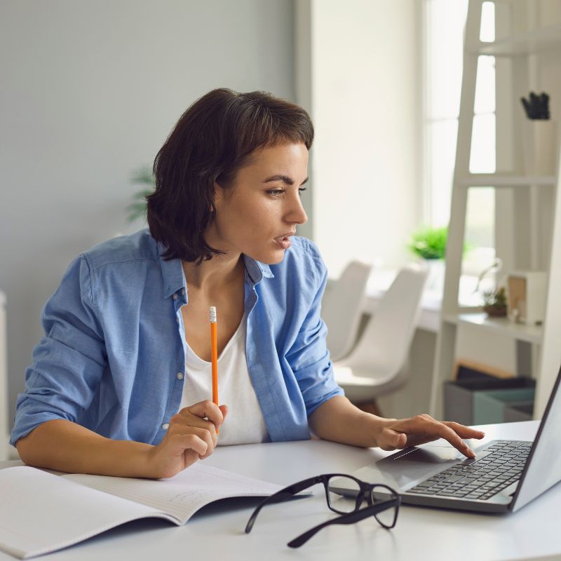 Woman focused on studying in front of her computer, taking notes.