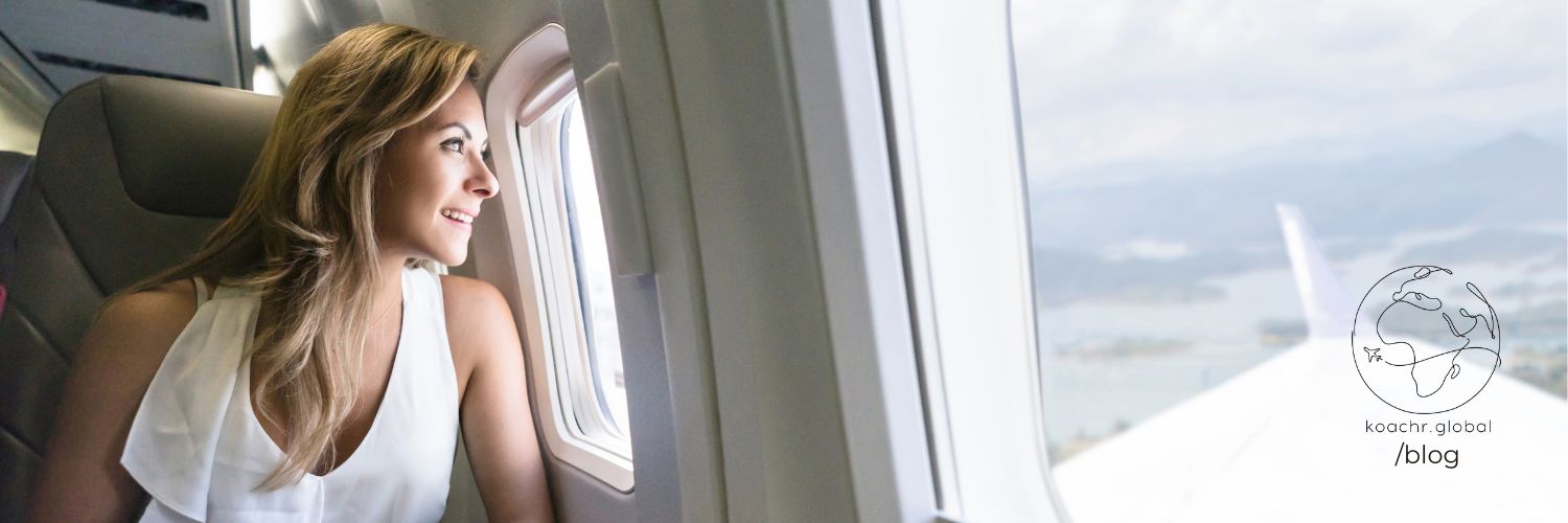 Woman peering out the window of a plane, looking excited about what's ahead.
