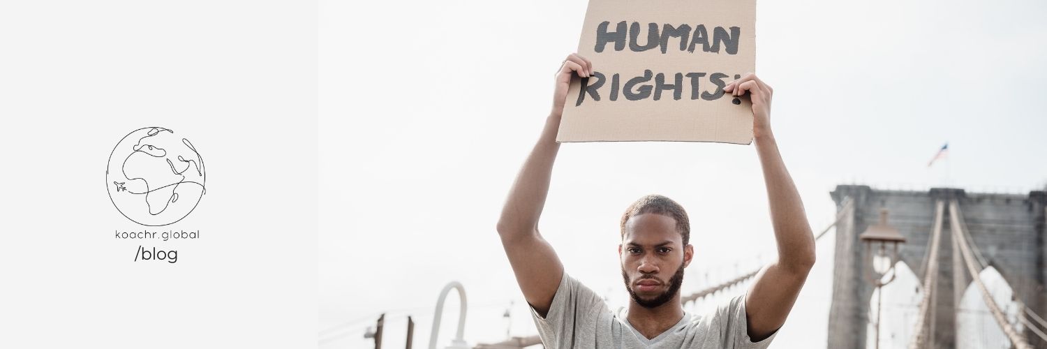 Serious-looking man holding up a hand-written sign saying "Human Rights", above his head.