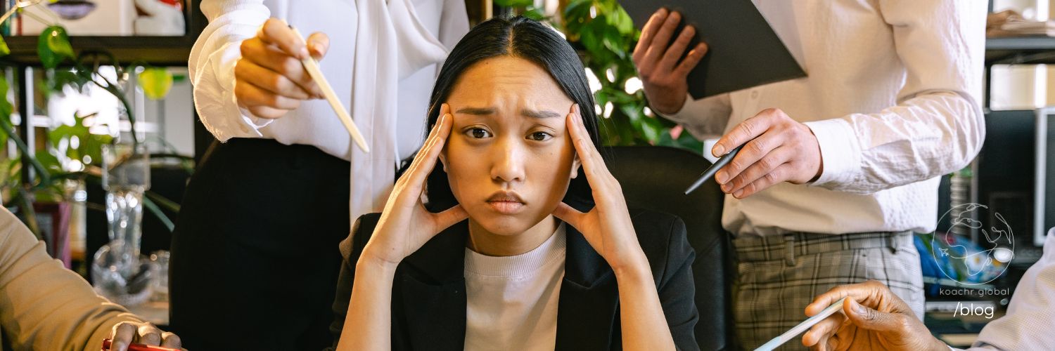 Woman at work holding her temples, looking pained from people around pressuring her.