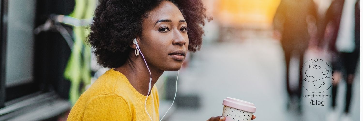 Woman gazing into the distance, absorbed in the podcast she's listening to, while sipping her cup of coffee.