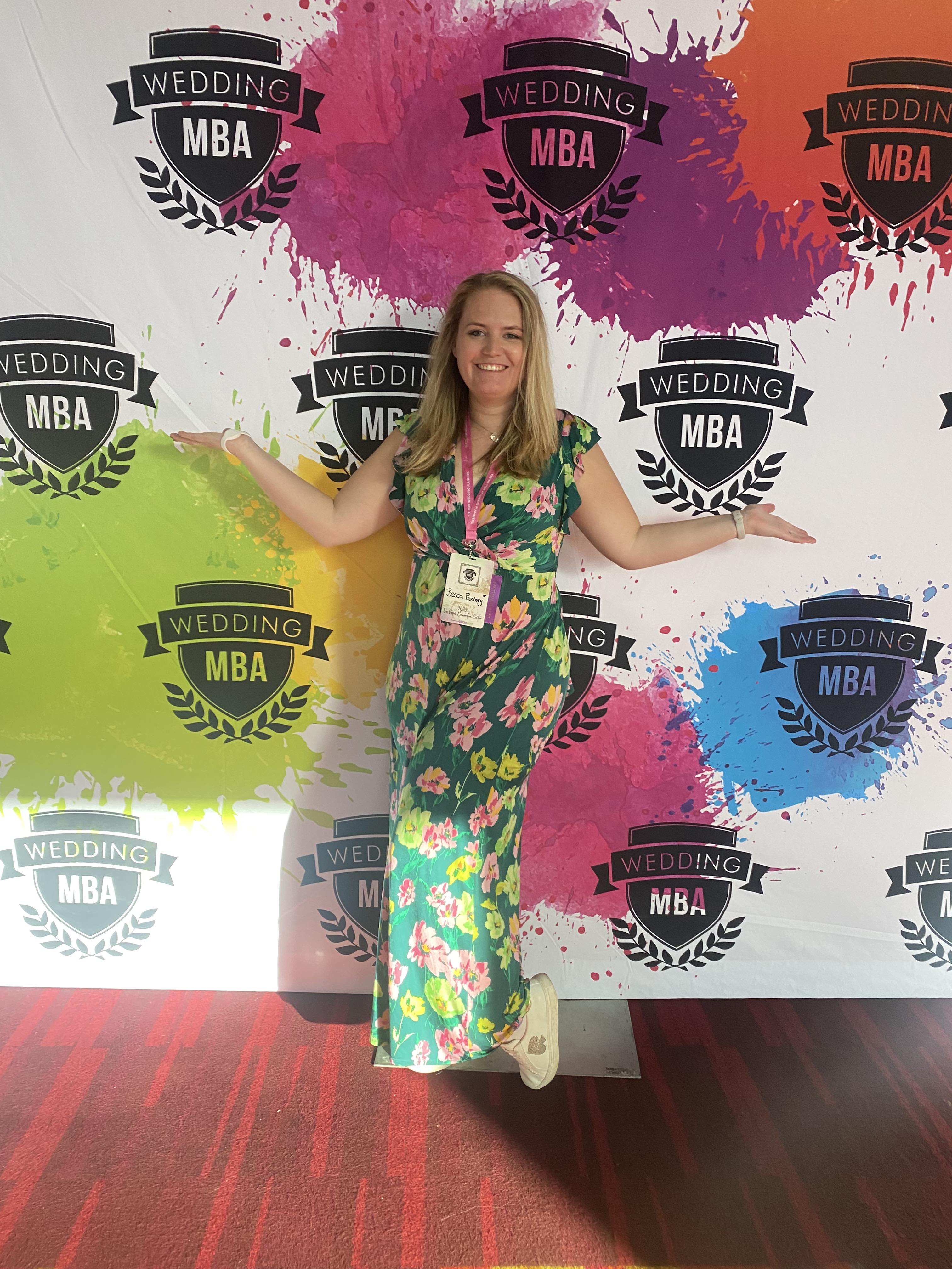 Becca Pountney at Wedding MBA 2023 in a green dress with flowers in front of a Wedding MBA logo wall