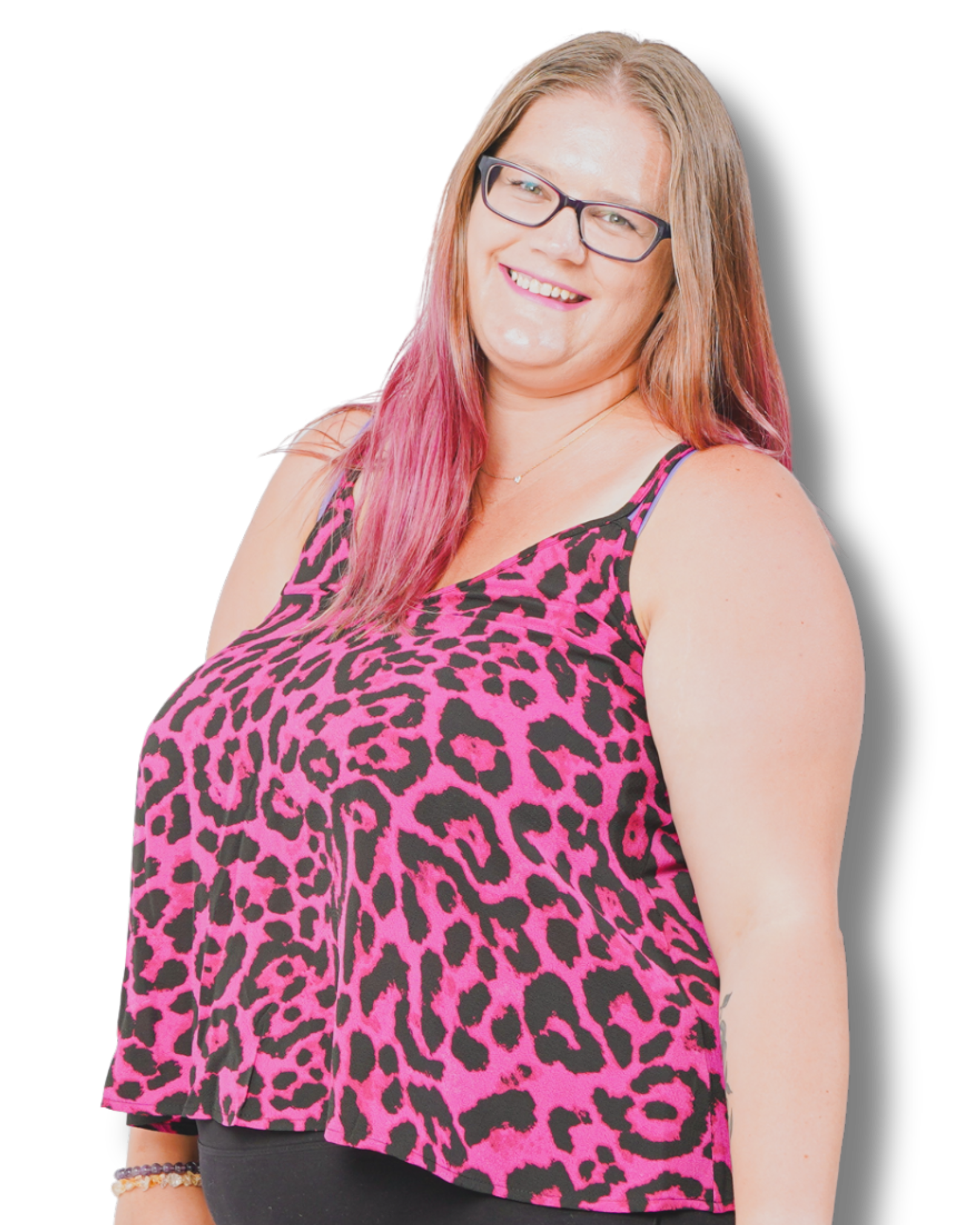 A business coach and mentor with pink-tinted hair works at her desk, smiling while writing in a notebook next to her laptop. 