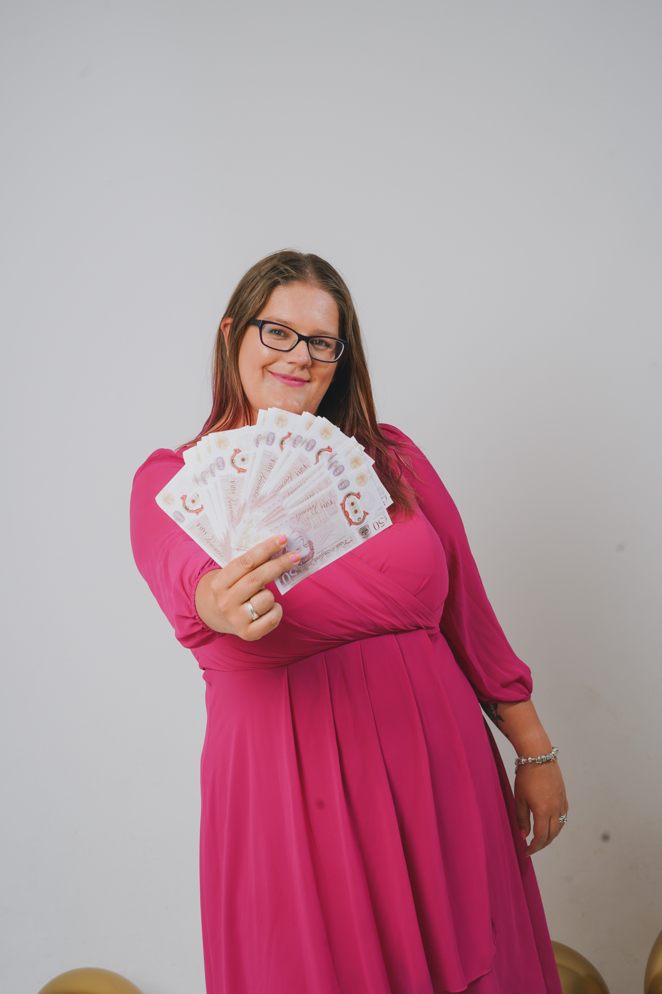 Dani wearing pink dress with fan of money held towards camera.png