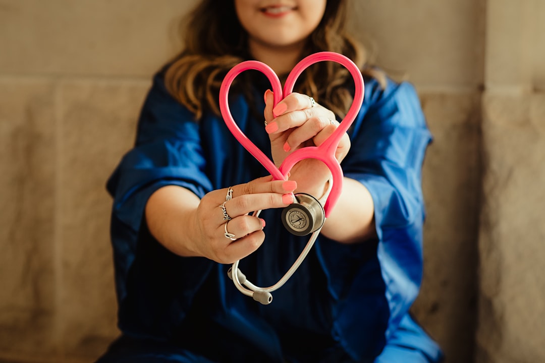 person in blue scrubs sitting on the floor, held out to the foreground of the photo is a stethoscope held in a heart shape.