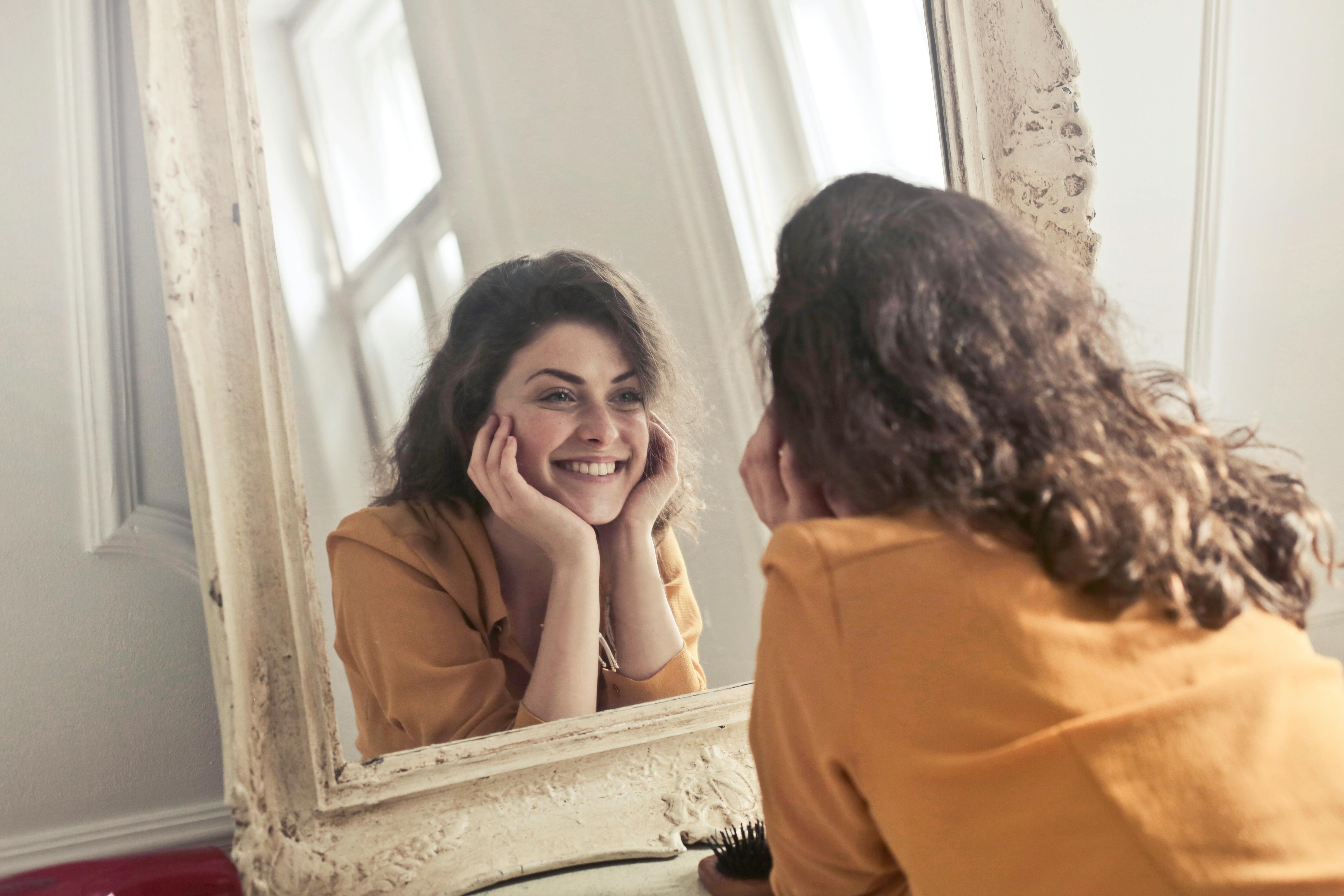 A midlife woman feeling happy looking in the mirror and liking herself