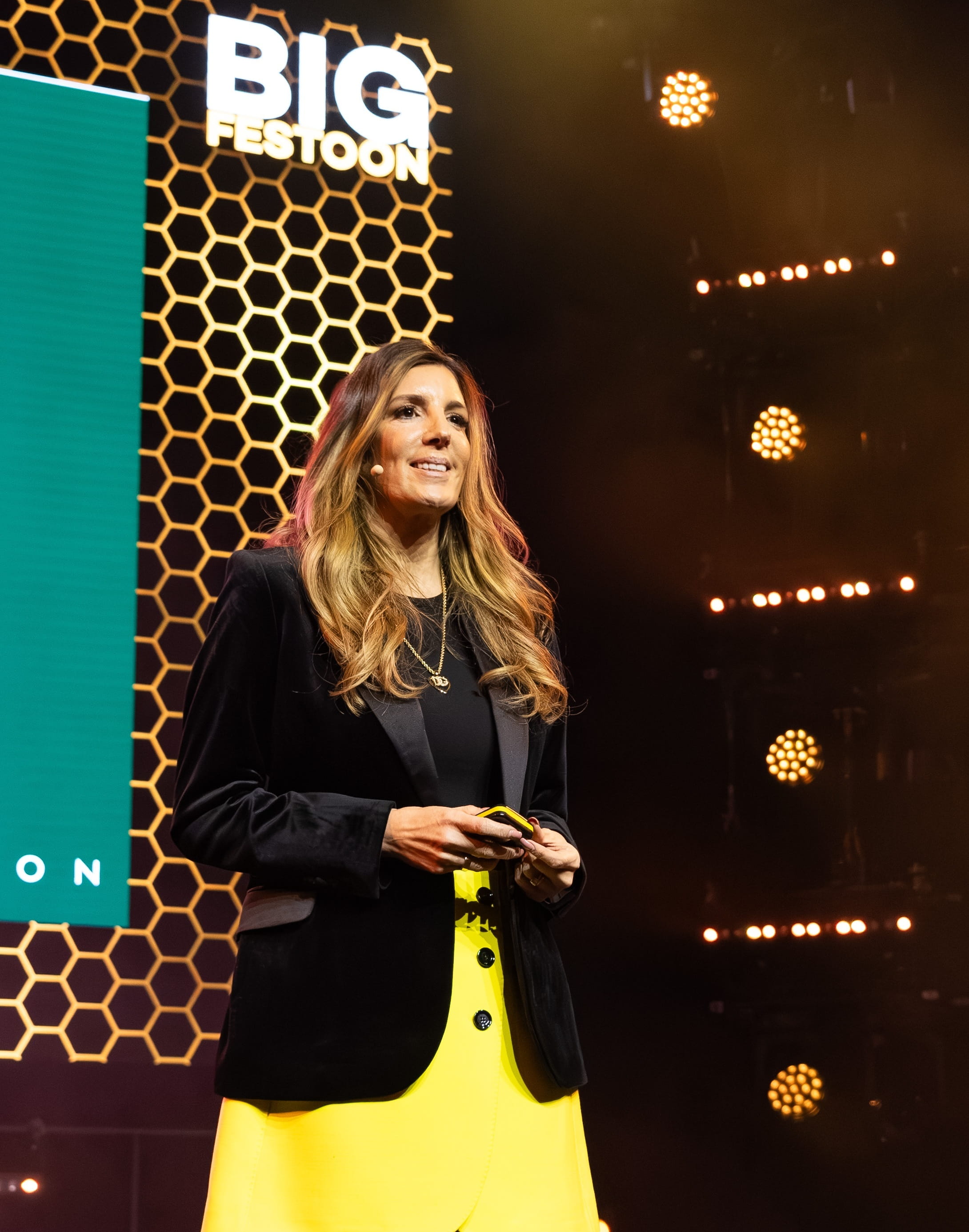 Lisa Johnson speaking at the Big Festoon event on a stage with honeycomb graphics and professional lighting.