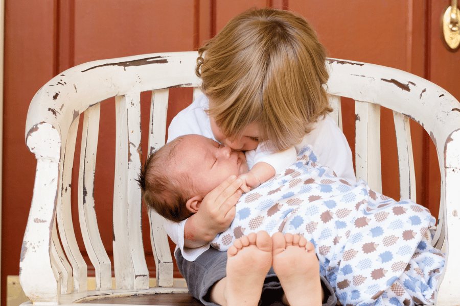 photo of little boy with newborn baby on his lap sitting outside on a wooden chair