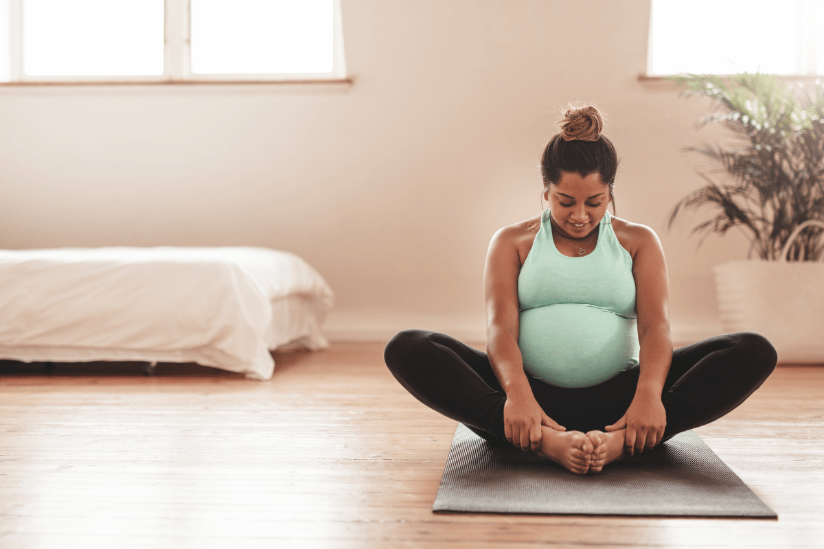 Image: pregnant woman sitting on a yoga mat, holding her feet