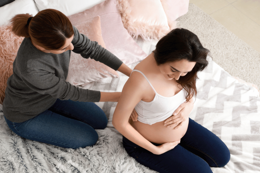 Image: woman giving pregnant woman back massage on bed.
