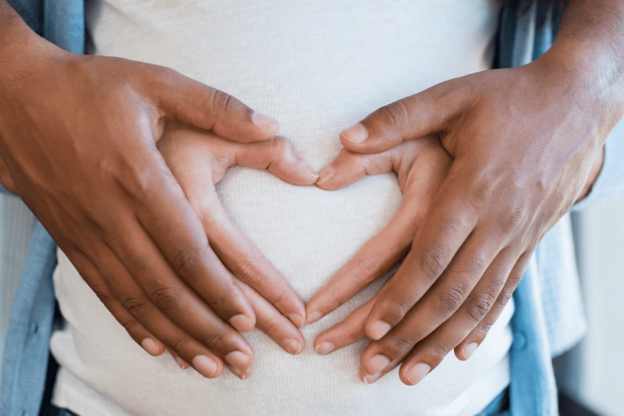 Photo of pregnant bump with white woman's hands and black mans hands making a heart shape