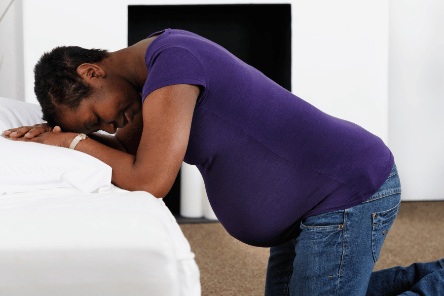photo of black pregnant woman on her knees leaning onto a white sofa