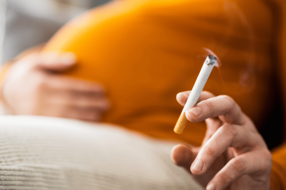 photo of woman's pregnant bump and hand holding a cigarette