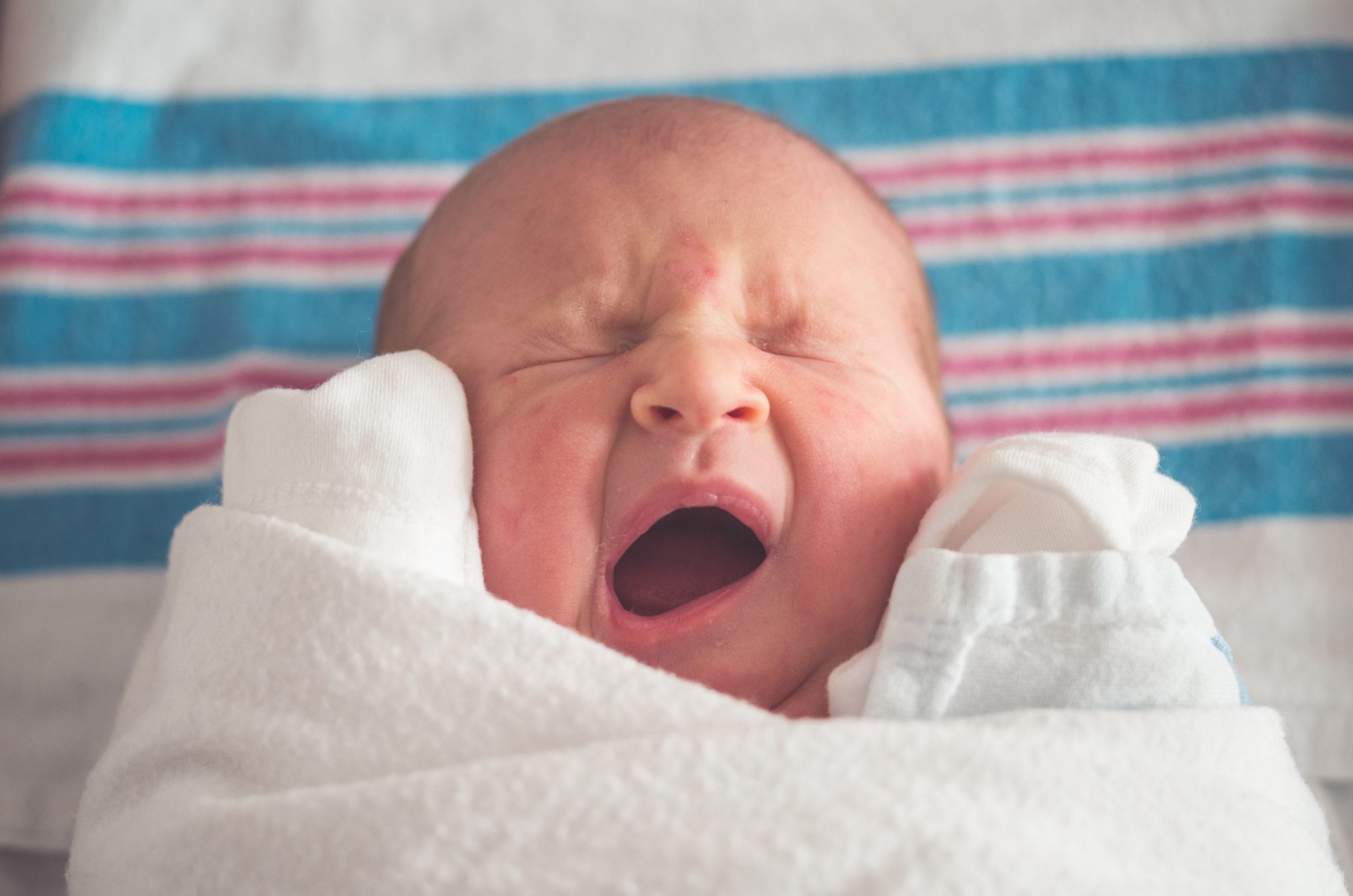 Photo of fussy baby in white clothing on a red, blue and white muslin.