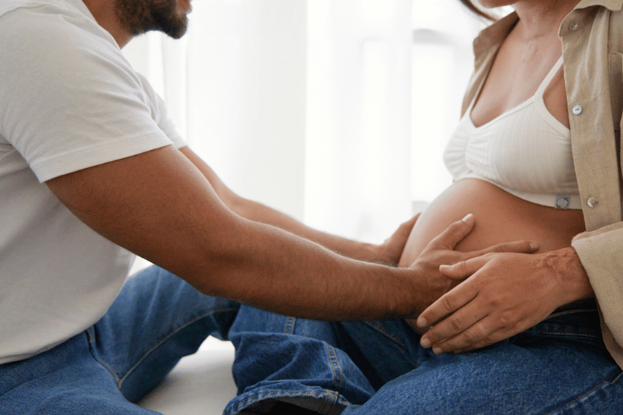 pregnant woman sitting cross legged on floor with partner touching her bump