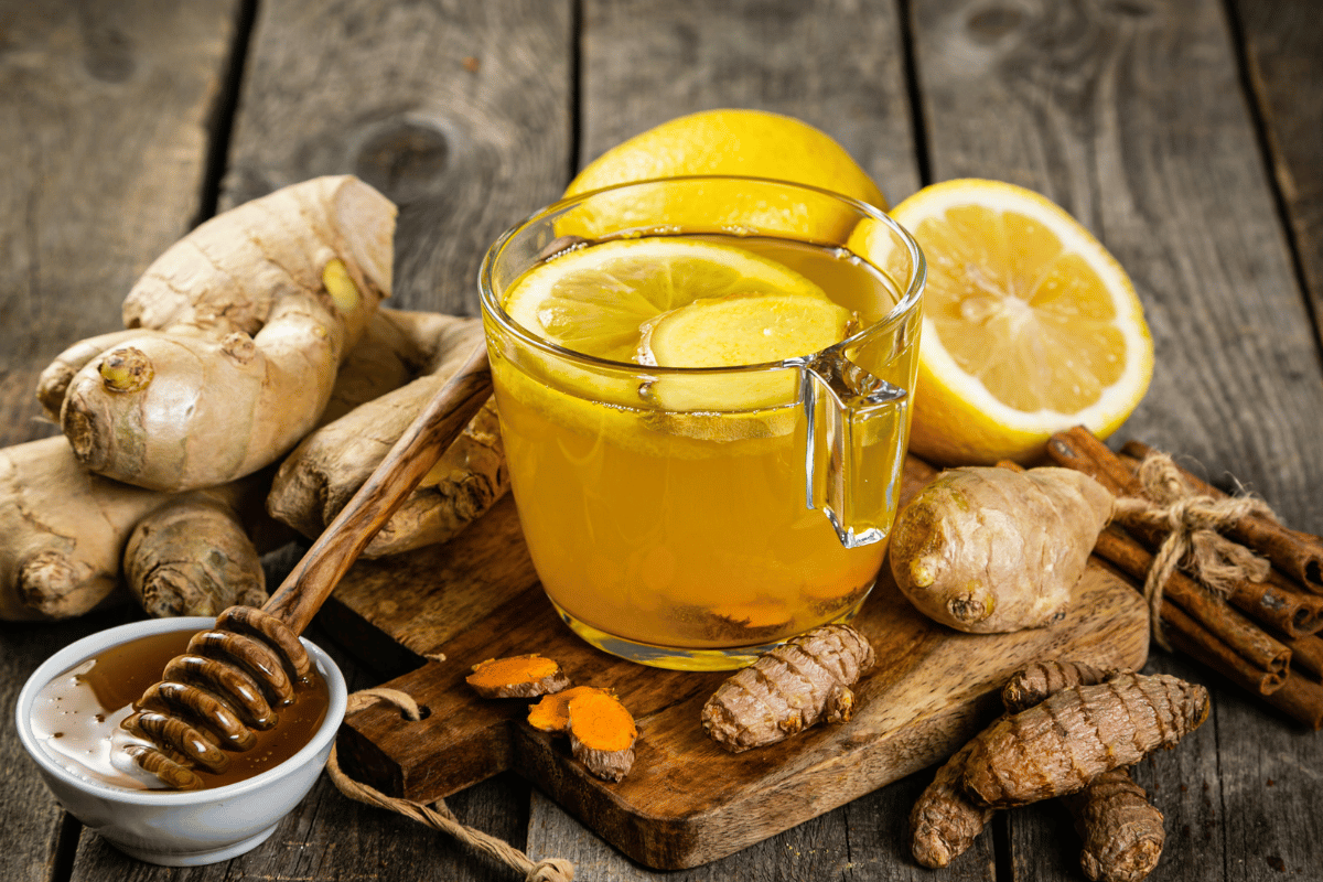 Photo of glass mug of lemon, ginger and honey with lemon, ginger and a bowl of honey next to it on the table