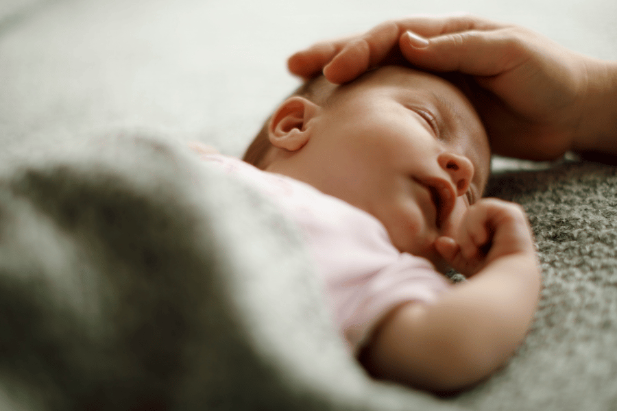 Baby asleep on their back with their mother's hand on their head