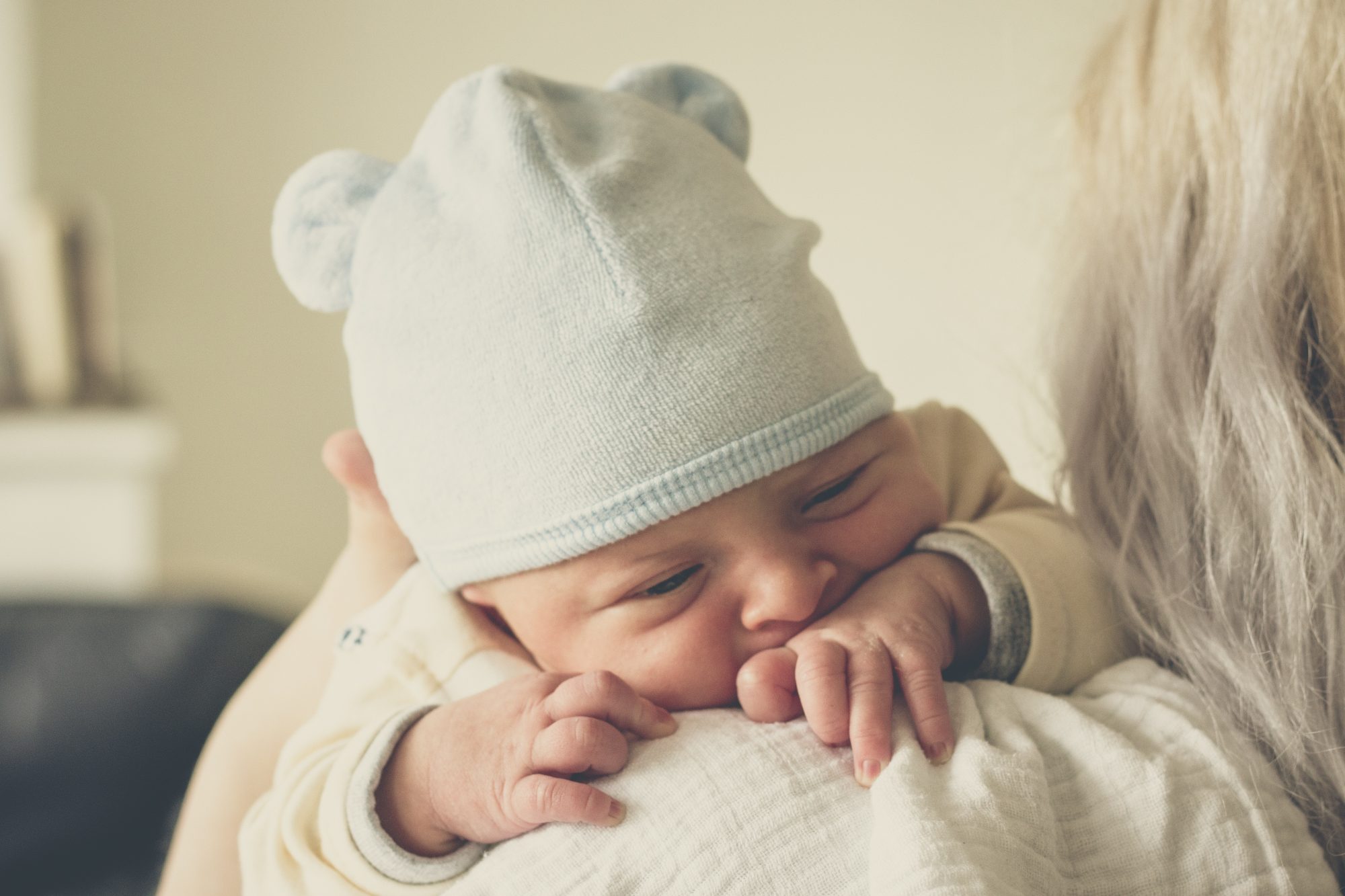 Photo of fussy baby sucking hand on mothers shoulder.