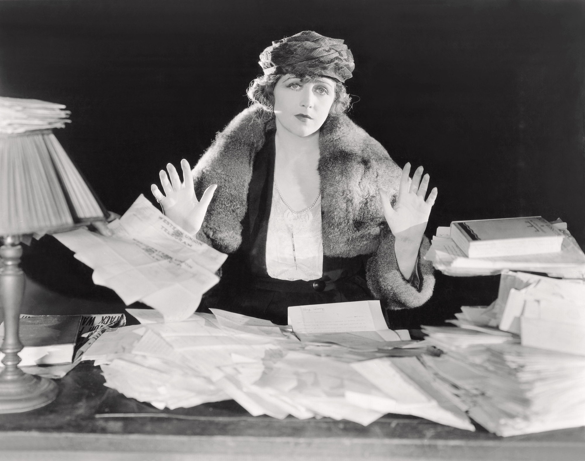 Black & white old-fashioned woman sitting at messy desk giving up