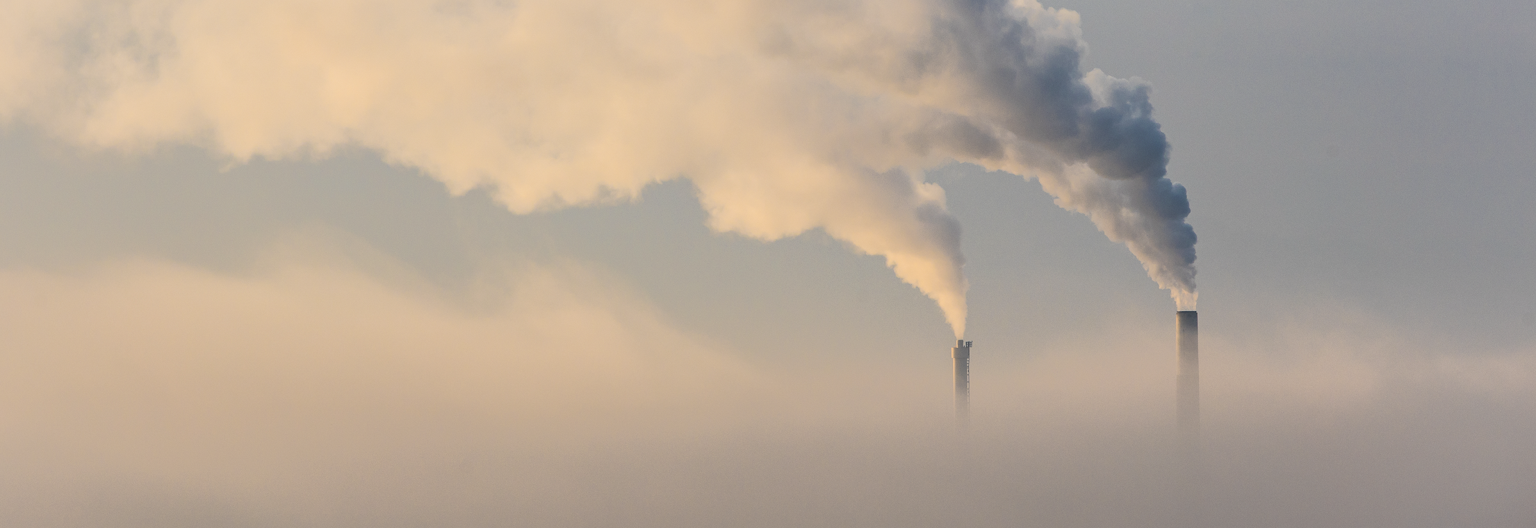 Two smog-billowing smoke stacks poke above dense clouds.