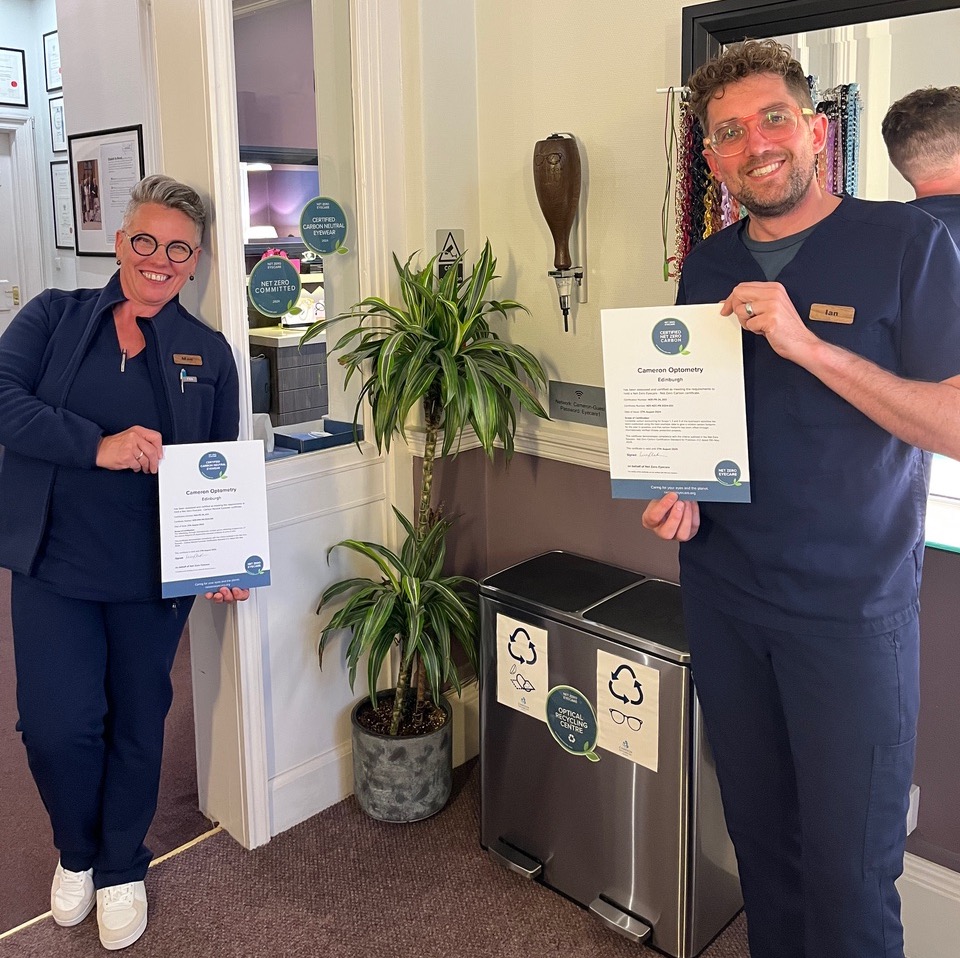 Two smiling opticians holding certificates in sustainability