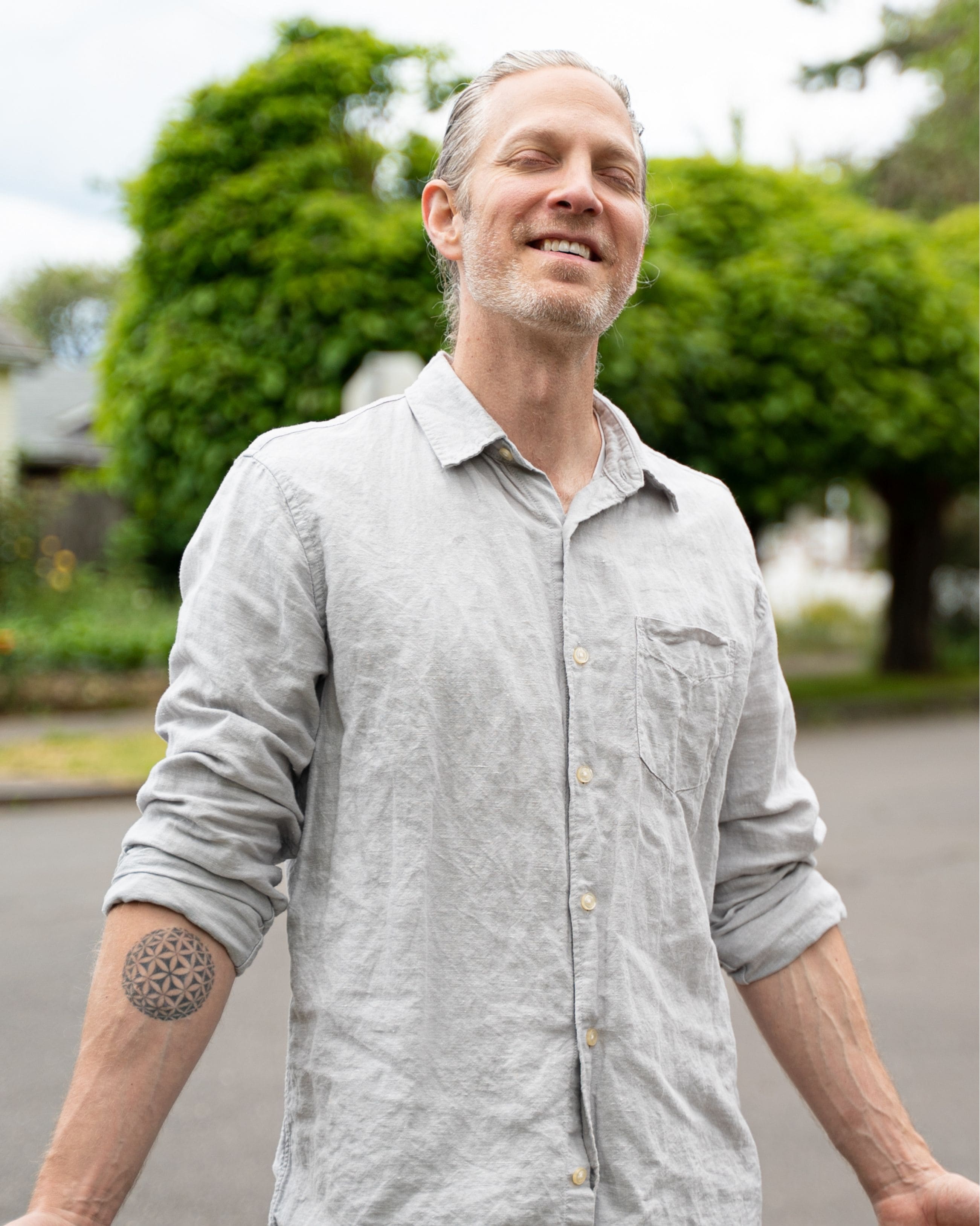 Person standing outdoors with eyes closed and a relaxed, peaceful expression