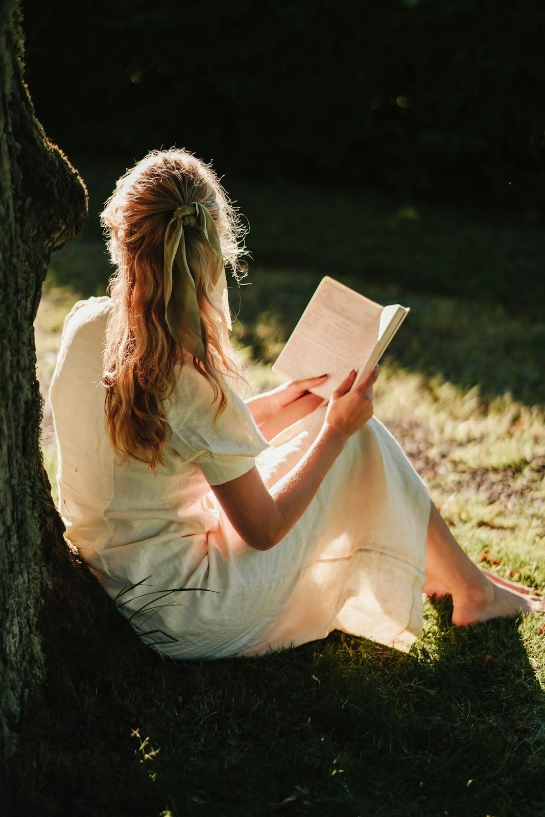 Girl sits by tree with book, representing self-discovery in personal growth retreats.