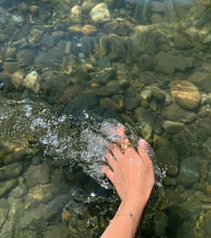 hand with gold ring and bracelet in water above rocks